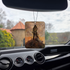 Frazetta Barbarian air freshener hanging in a car with black interior. The Frazetta Art Museum sits in the background with gloomy clouds overhead.