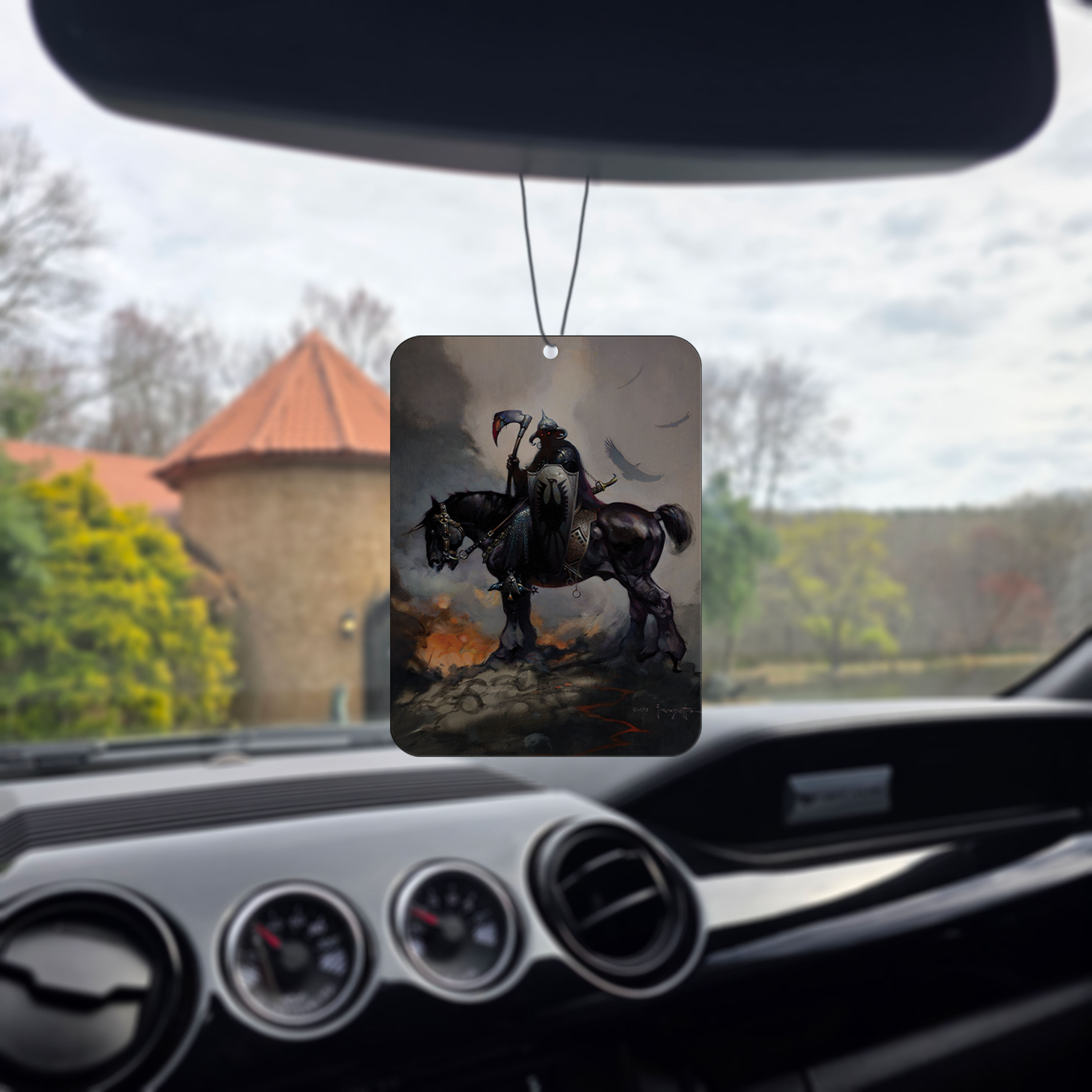 Frazetta Death Dealer I air freshener hanging in a car with black interior. The Frazetta Art Museum sits in the background with gloomy clouds overhead.