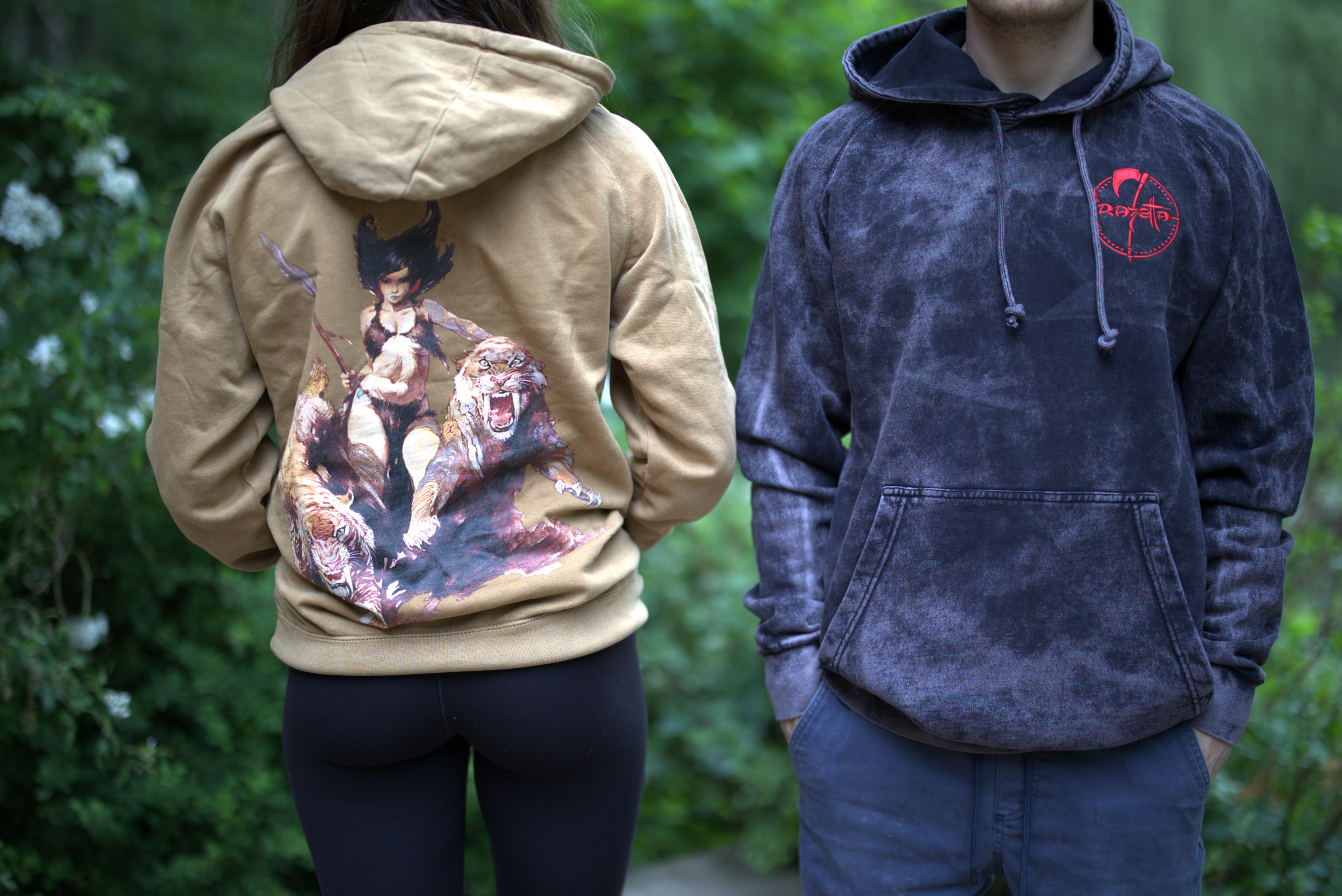 A man and a woman wearing premium cotton Frazetta hoodies featuring Frazetta's iconic fantasy works.