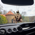 Frazetta Huntress air freshener hanging in a car with black interior. The Frazetta Art Museum sits in the background with gloomy clouds overhead.