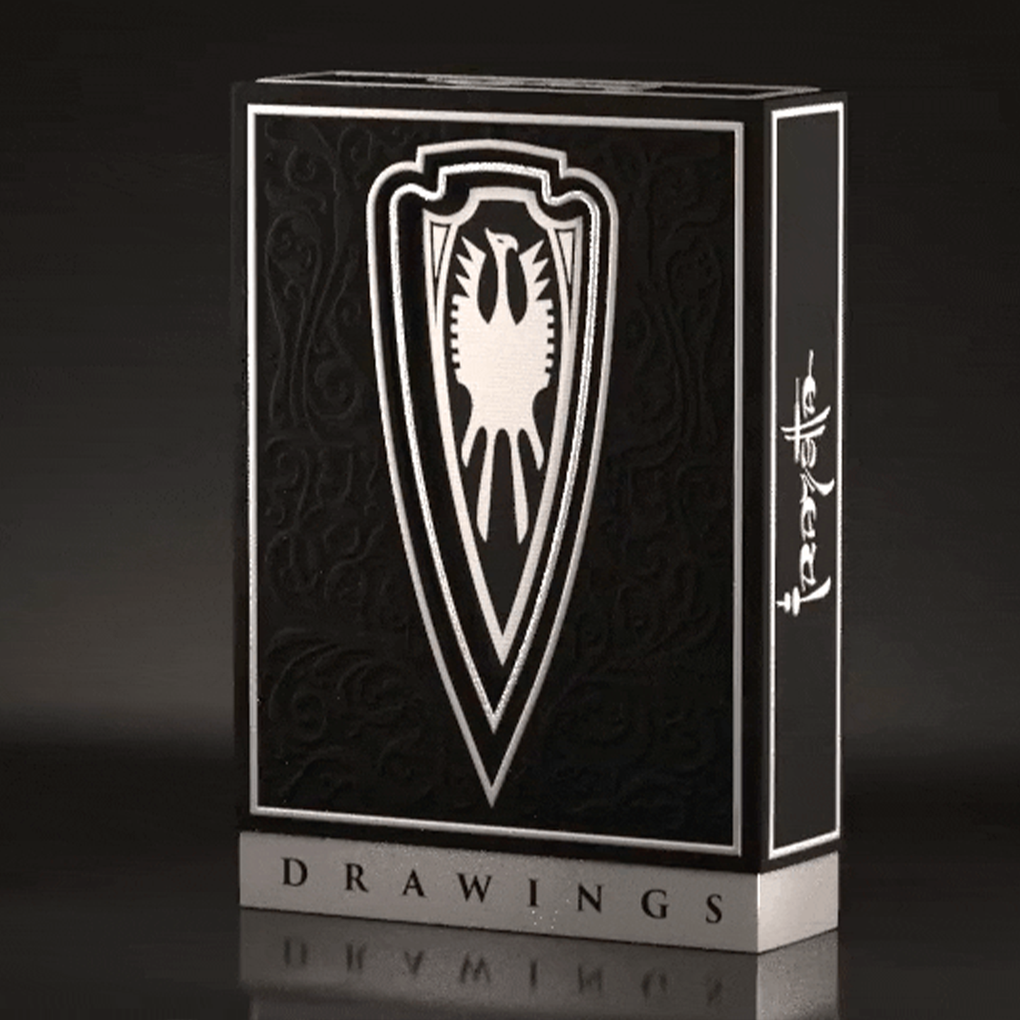 A high-end playing card deck from the Frazetta Drawings Edition is displayed against a sleek, dark background. The black tuck box features intricate embossing, silver foil accents, and a bold shield emblem with a stylized eagle at its center. The side of the box is adorned with the Frazetta signature, enhancing its luxury and collector’s appeal. The reflective silver details catch the light, emphasizing the deck’s premium craftsmanship.