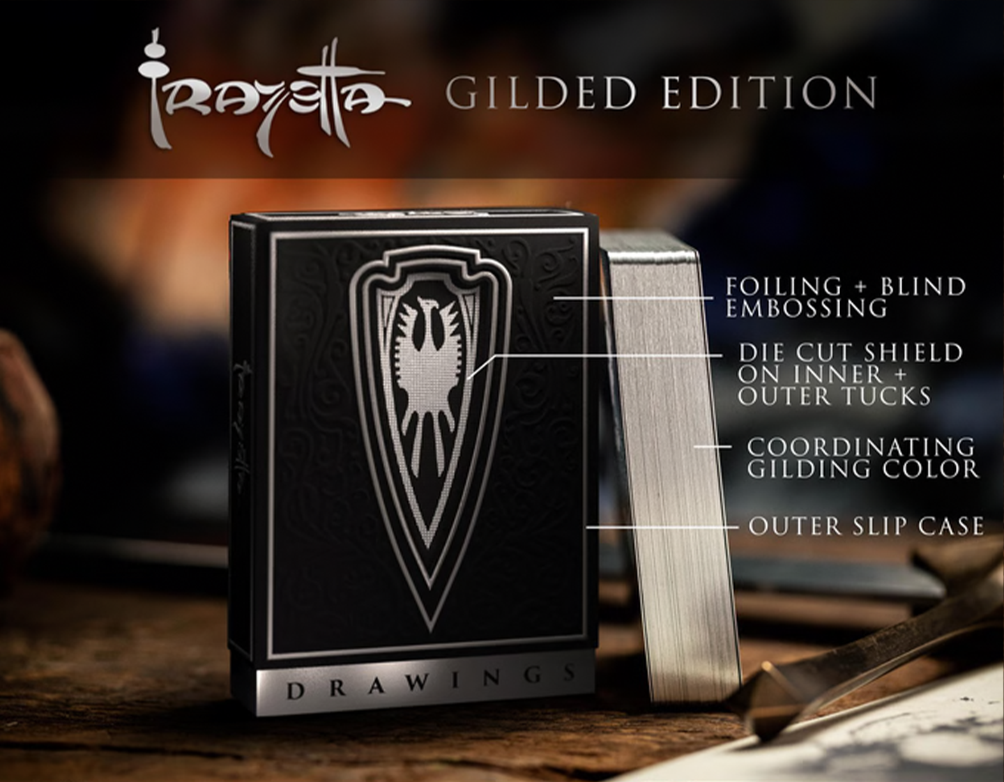 A Gilded Edition playing card deck from the Frazetta collection is displayed on a rustic wooden surface. The "Drawings" deck features a sleek black tuck box with silver foiling, blind embossing, and an intricately designed shield emblem. Beside it, the deck’s coordinating silver-gilded edges add a premium touch. Overlayed text highlights the deck’s luxury features, including a die-cut shield on the inner and outer tucks, foiling details, and an outer slipcase for added protection.