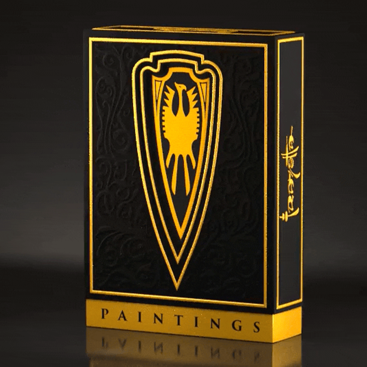 A high-end playing card deck from the Frazetta Paintings Edition is displayed against a sleek, dark background. The black tuck box features intricate embossing, gold foil accents, and a bold shield emblem with a stylized eagle at its center. The side of the box is adorned with the Frazetta signature, enhancing its luxury and collector’s appeal. The reflective gold details catch the light, emphasizing the deck’s premium craftsmanship.