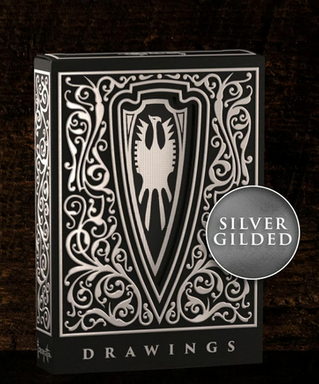 A luxurious black and silver playing card box featuring an intricate, ornate design. The front showcases a bold shield emblem with a stylized eagle at its center, surrounded by elegant filigree patterns. The box is set against a dark, textured wooden background, emphasizing its premium craftsmanship and collectible nature.