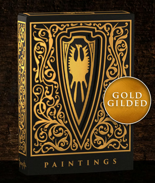 A luxurious black and gold playing card box featuring an intricate, ornate design. The front showcases a bold shield emblem with a stylized eagle at its center, surrounded by elegant filigree patterns. The box is set against a dark, textured wooden background, emphasizing its premium craftsmanship and collectible nature.