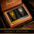A luxurious wooden collector’s box holds two elegantly designed playing card decks from the Legacy Edition set. The "Paintings" deck, in black and gold, and the "Drawings" deck, in black and silver, feature intricate shield emblems and ornate detailing. The Frazetta logo is engraved on the inside of the wooden lid, adding to the premium presentation. The set rests on a rich wooden surface, surrounded by dark-toned accessories, emphasizing its collector’s appeal and craftsmanship.