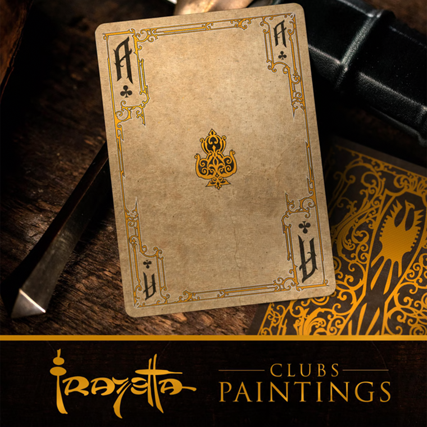 A close-up of an Ace of Clubs from the Frazetta Paintings Edition playing card deck. The card features an ornate, vintage-style border with delicate filigree and a stylized club symbol at its center. Beneath it, additional cards are partially visible, showcasing intricate artwork and embossed detailing. A knife rests nearby, enhancing the dramatic composition.