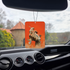 Photo of the Frazetta Reassembled Man air freshener hanging in a car with black interior. The Frazetta Art Museum sits in the background with gloomy clouds overhead.