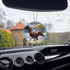 Photo of the Frazetta Wild Ride air freshener hanging in a car with black interior. The Frazetta Art Museum sits in the background with gloomy clouds overhead.