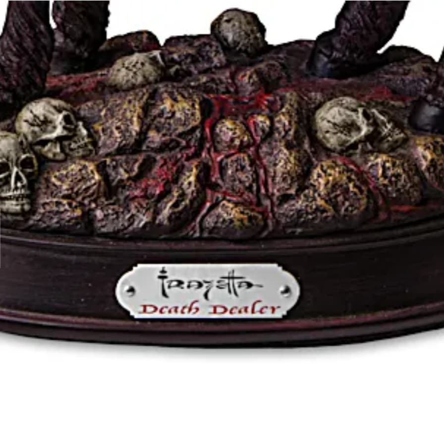 A close-up of the Death Dealer sculpture’s base, featuring a blood-stained rocky terrain strewn with skulls. The metallic nameplate on the wooden base bears the Frazetta signature and "Death Dealer" in bold lettering.