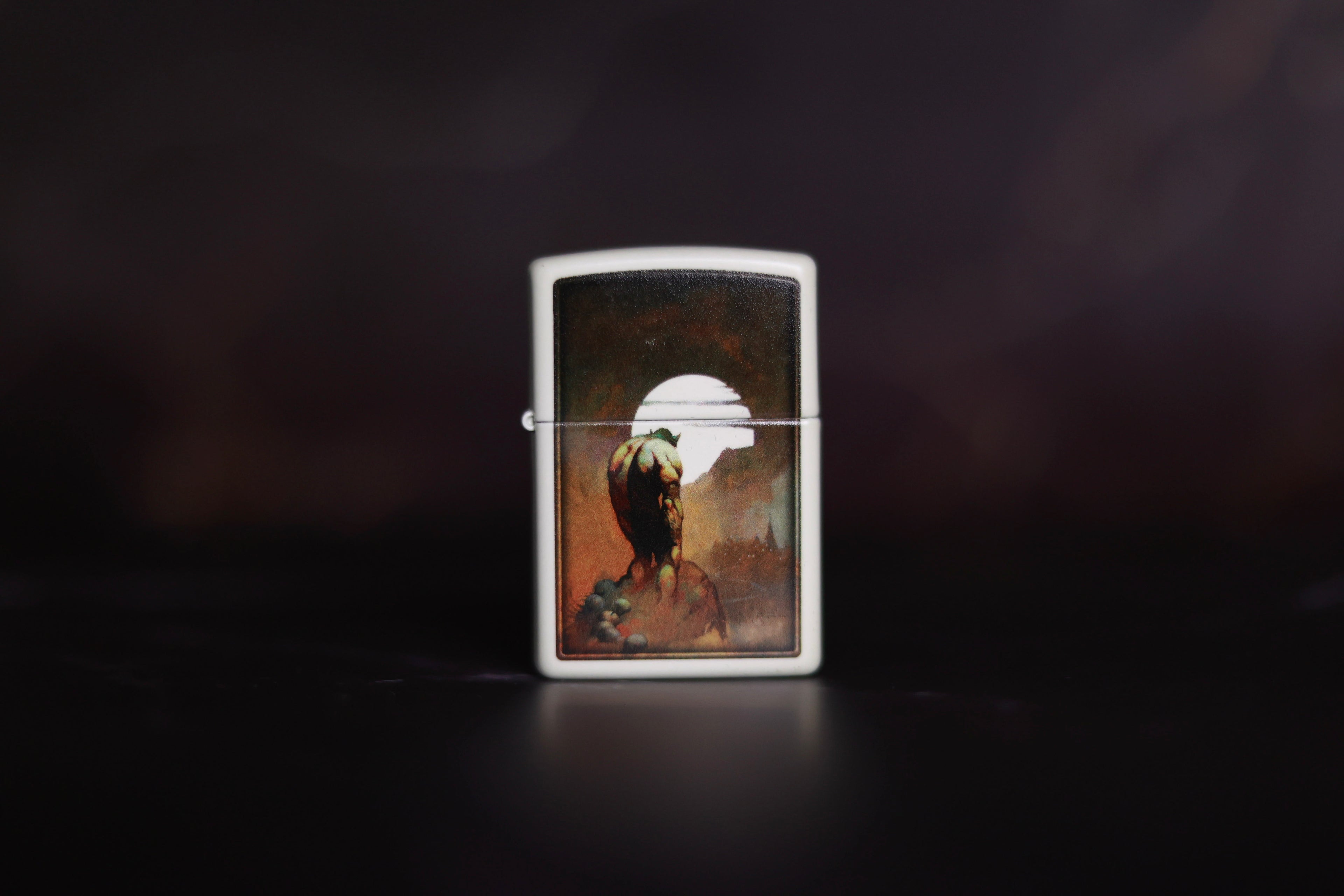 Zippo lighter featuring Frank Frazetta’s Night Stalker artwork, showing a muscular figure standing before a glowing full moon over a darkened town.