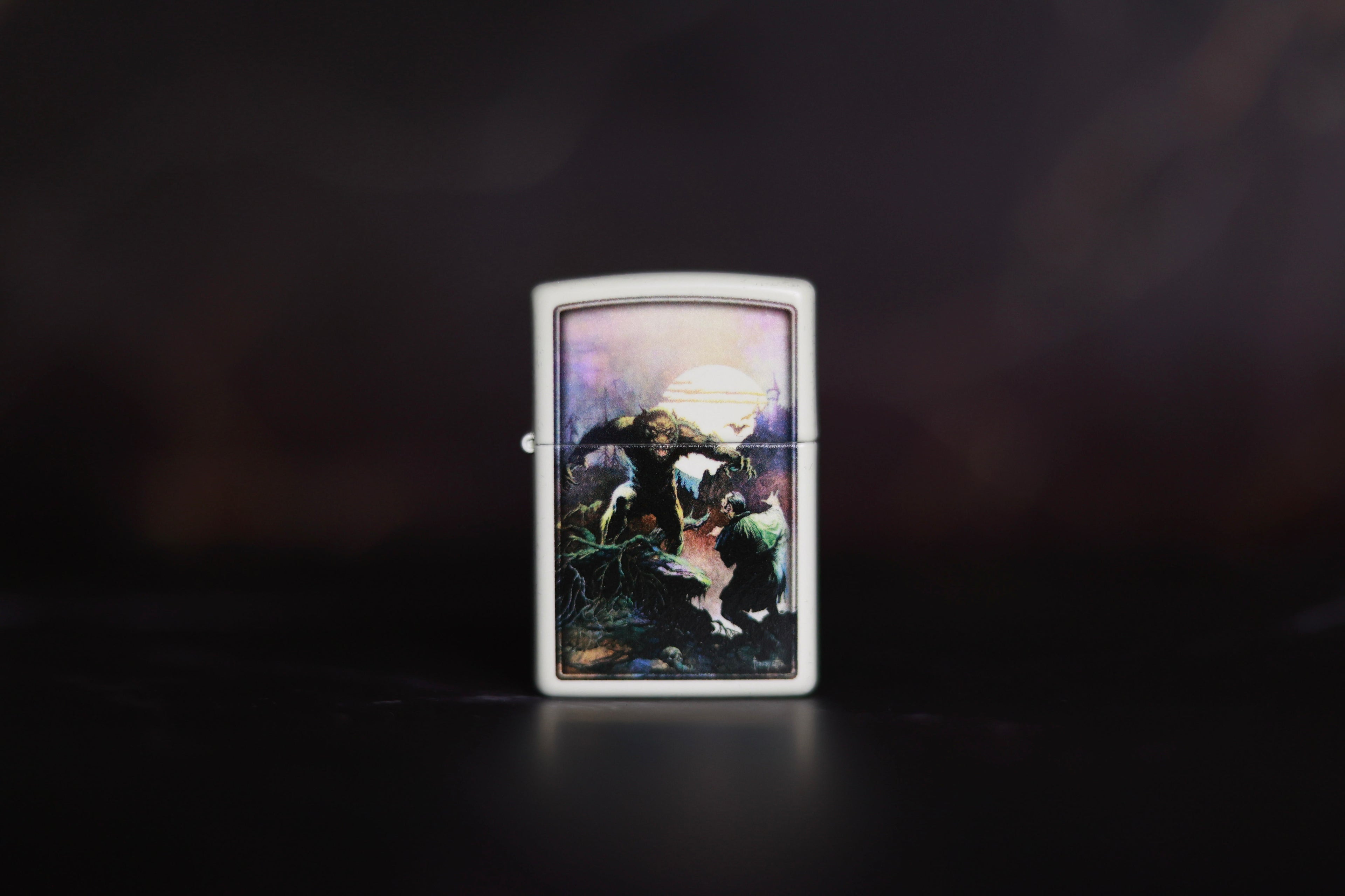White Zippo-style lighter featuring Frank Frazetta’s artwork Wolfmoon, depicting a werewolf-like creature under a glowing full moon, confronting a cloaked figure amid a dark, moody landscape.