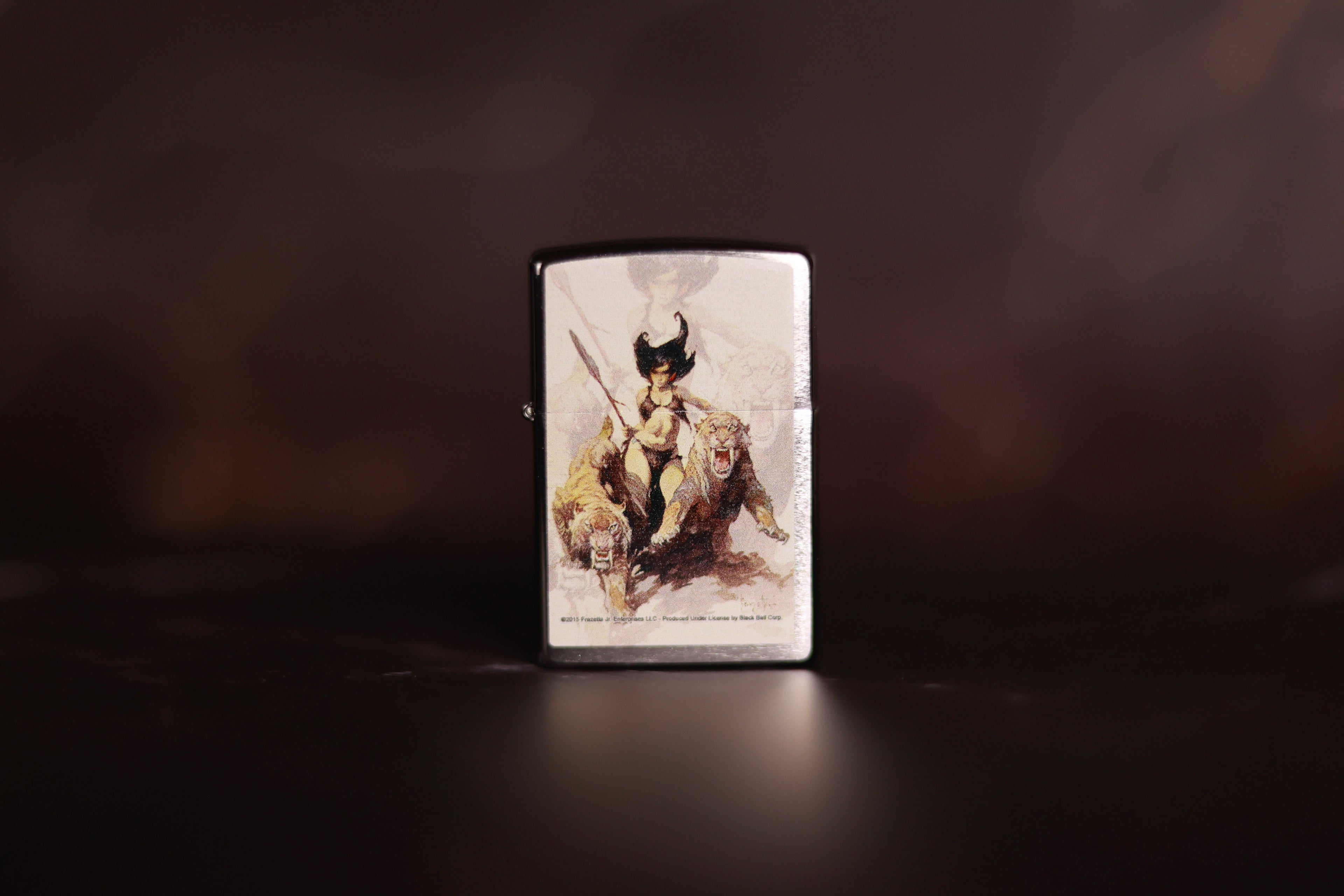 Zippo lighter featuring Frank Frazetta’s The Huntress artwork, depicting a fierce warrior woman standing between two saber-toothed cats against a pale backdrop.
