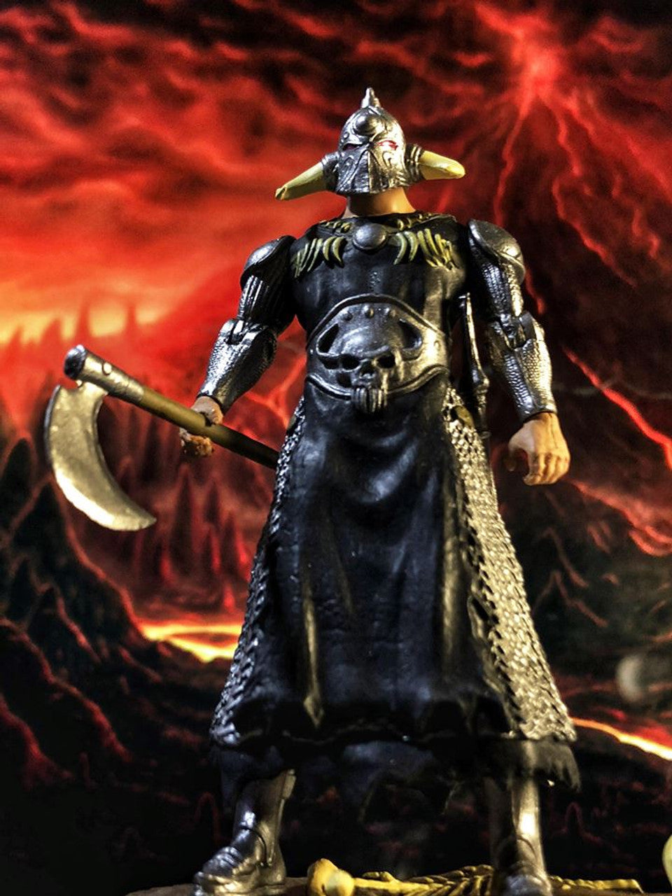 A 3.75” scale retro action figure of Frank Frazetta’s Death Dealer stands on a detailed blood, bones, and stone display base. The figure features heavy armor with chain mail sleeves, a long-horned helmet, and comes equipped with a battle-worn axe and shield, which fits into the skull-adorned base.