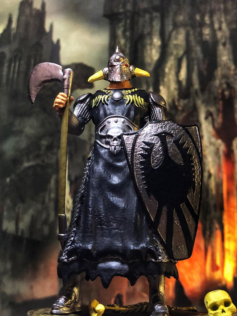A 3.75” scale retro action figure of Frank Frazetta’s Death Dealer stands on a detailed blood, bones, and stone display base. The figure features heavy armor with chain mail sleeves, a long-horned helmet, and comes equipped with a battle-worn axe and shield, which fits into the skull-adorned base.