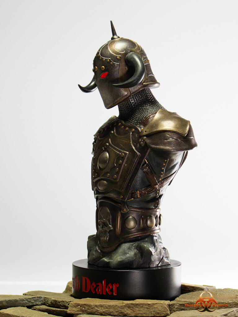 A side profile view of the 1/4 scale Death Dealer bust, showcasing intricate armor detailing, a horned helmet, and glowing red eyes. The statue sits on a black base inscribed with "Death Dealer" in bold red lettering, set against a neutral background.