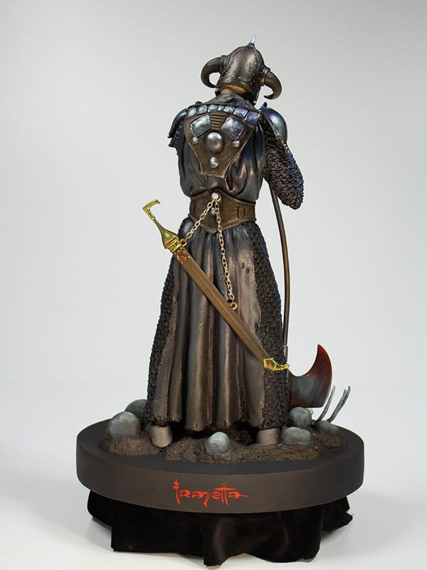 Rear view of the Death Dealer 1:6 scale statue by Quarantine Studio, showcasing intricate armor detailing, a sheathed sword with gold accents, and flowing chainmail. The warrior stands on a battlefield base adorned with skulls and debris, with Frazetta’s signature displayed on the base.