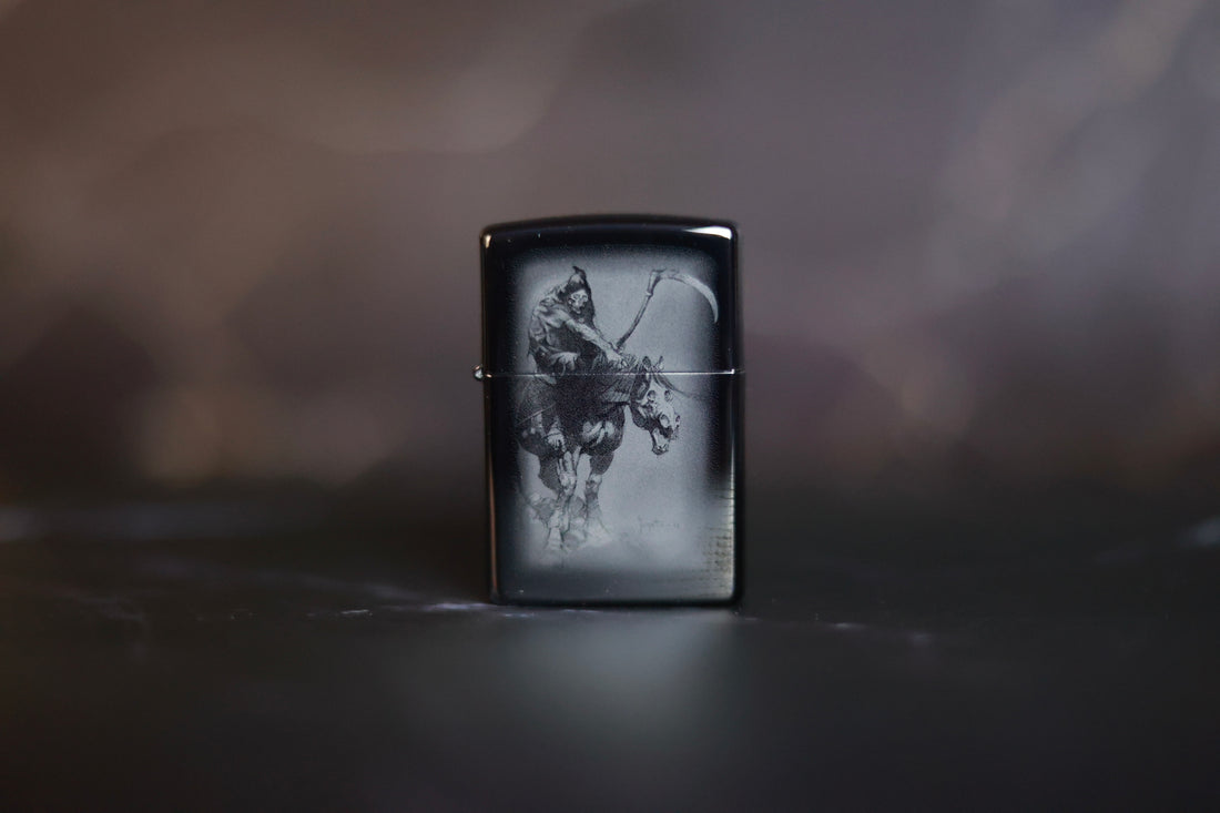 Black Zippo-style lighter featuring Frank Frazetta’s Grim Reaper artwork etched in grayscale, displayed upright on a dark, blurred background.